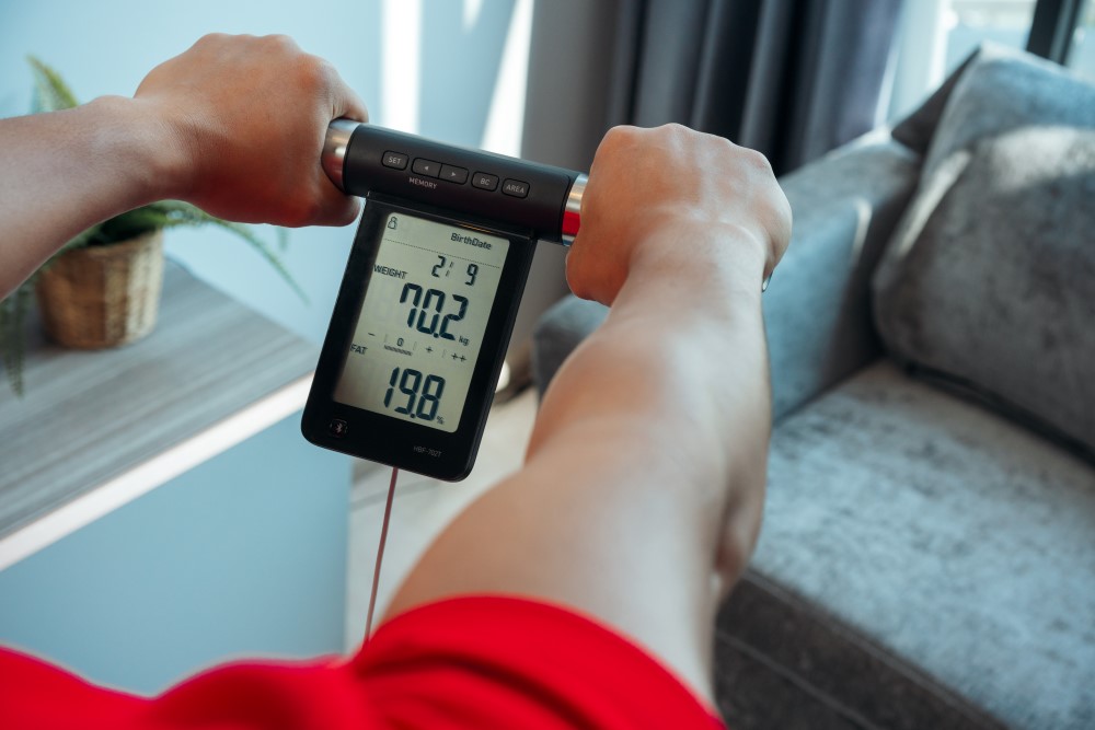 A person is using a body composition monitor to measure his body weight and fat.