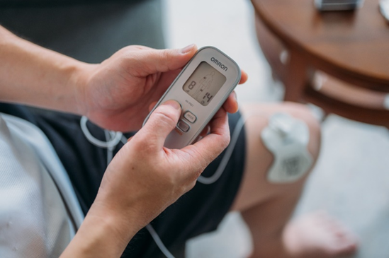 Person using OMRON TENS pain relief device to relieve knee pain